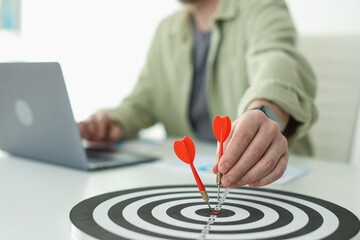 Man with dart aiming at dartboard while working indoors, closeup