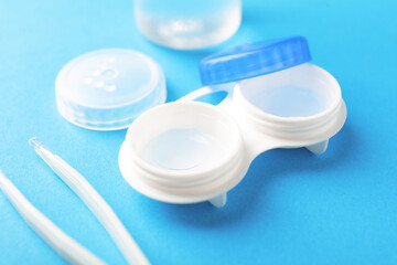 Contact lenses in case and tweezers on light blue background, closeup
