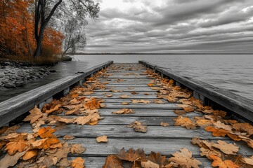 Autumn leaves on a wooden dock extending to a tranquil lake under a cloudy sky.