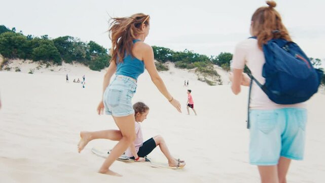 Family sandboarding. Girl glides down the sand dune