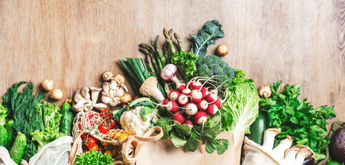 Food background. Healthy vegan eating, cooking  banner. Eco fiendly shopping bags with fresh vegetables, herbs, mushrooms, asparagus, radish on wooden table
