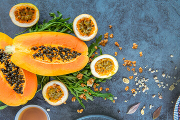 Slices of sweet papaya, passion fruit and rucola surrounded by granola flakes on a stone background