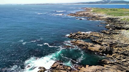 A stunning coastal landscape features a rocky shoreline next to clear, sparkling blue waters