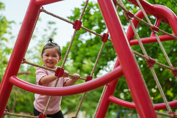 happy toddler girl playing with climbing ropes net at a outdoor playground in park