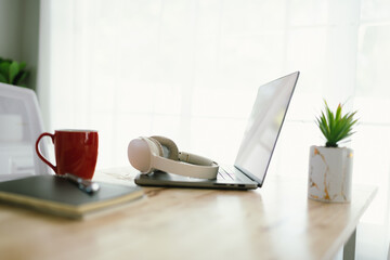 A modern, minimalist desk workspace with a laptop, headphones, notepad, cup of coffee, and houseplant, ready for productive remote work.