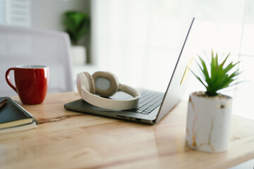 A modern, minimalist desk workspace with a laptop, headphones, notepad, cup of coffee, and houseplant, ready for productive remote work.