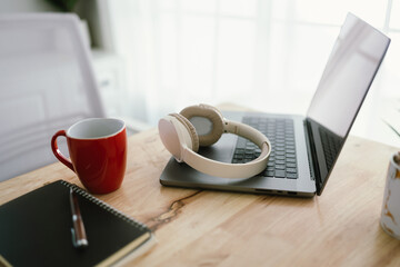A modern, minimalist desk workspace with a laptop, headphones, notepad, cup of coffee, and houseplant, ready for productive remote work.