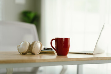 A modern, minimalist desk workspace with a laptop, headphones, notepad, cup of coffee, and houseplant, ready for productive remote work.