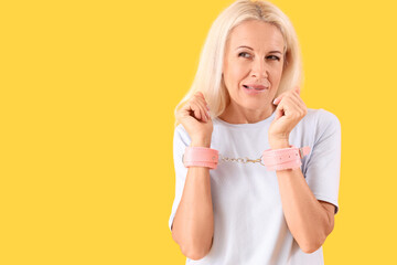 Mature woman with handcuffs from sex shop on yellow background