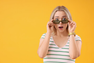 Shocked young beautiful woman in stylish sunglasses on yellow background