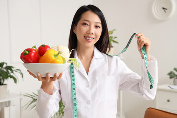 Female Asian nutritionist with healthy food and tape measure in office