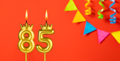 Number 85 candle - Birthday celebration on an orange background with pennants