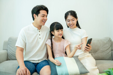 Obraz premium Asian family using a smartphone. The little girl is pointing at the screen, showing something interesting to her parents.