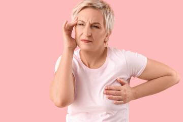 Beautiful mature woman suffering from breast pain on pink background. Cancer awareness concept