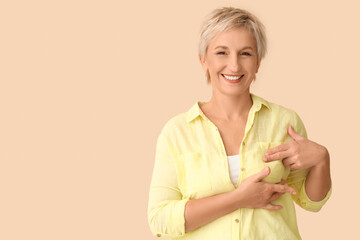 Beautiful mature woman checking her breast on beige background. Cancer awareness concept