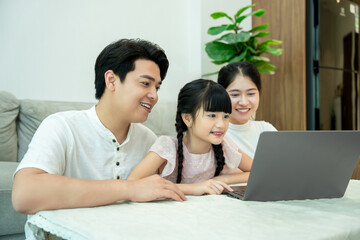 Fototapeta premium Asian family enjoys spending time together online, smiling as they look at a laptop screen.