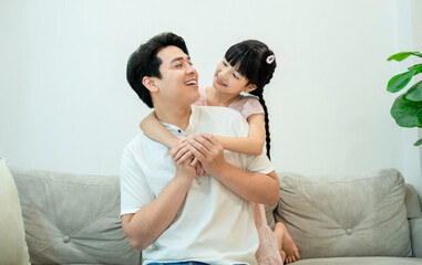 A sweet, candid moment of a young girl hugging her father from behind as they look at each other...