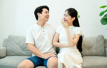 	 young asian couple sitting on sofa talking happily 