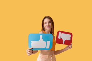 Pretty young woman holding like and dislike icons on orange background