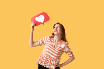 Pretty young woman holding heart like icon on orange background
