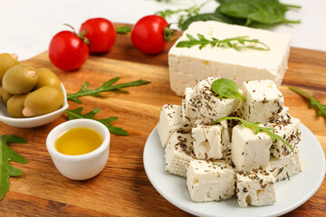 Wooden board and plate with delicious cut feta cheese on light background