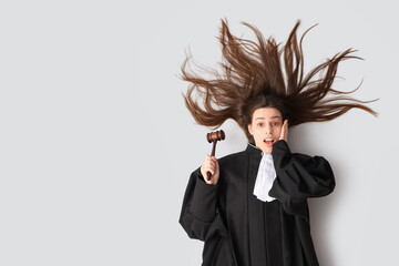 Surprised young female judge with gavel lying on white background