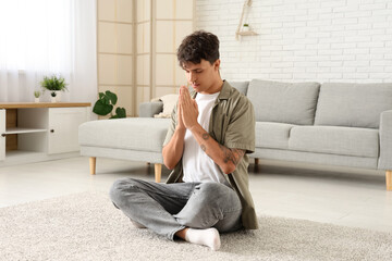 Young man praying and sitting in living room