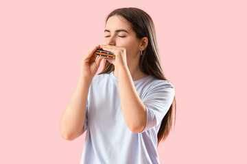 Young woman playing harmonica on pink background