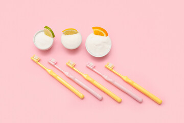 Bowls of tooth powder with citrus slices and brushes on pink background. Top view