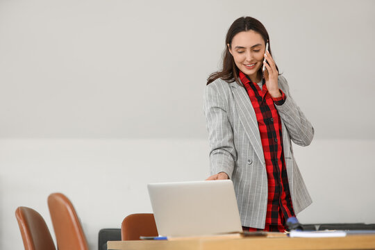 Young businesswoman talking by mobile phone at table in office. National Wear Your Pajamas to Work Day