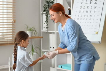 Female ophthalmologist giving contact lenses to little girl in clinic