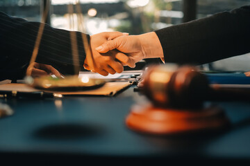 Two lawyers shaking hands after reaching an agreement during a legal trial, with scales of justice and gavel in the foreground