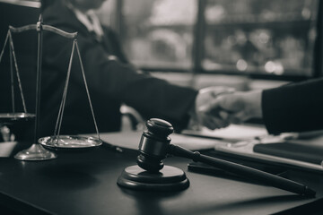Two lawyers shaking hands after reaching an agreement during a legal trial, with scales of justice and gavel in the foreground