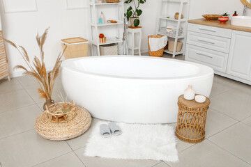 Interior of modern bathroom with bathtub and soft slippers on fluffy rug