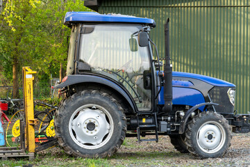 Fototapeta premium Blue Farm Tractor Parked on Gravel Surface with Attached Agricultural Equipment
