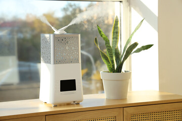 Modern air humidifier with plant on commode near window in room