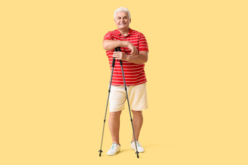 Sporty senior man with walking poles on yellow background