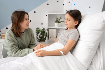 Fototapeta premium Cute girl with infusion drip and her mother in hospital room