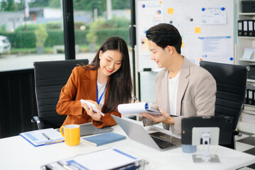 Two young Asian professionals engaged in teamwork and business discussions in modern office