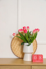 Cube calendar with date of Women's Day and tulips in vase on commode near light wall