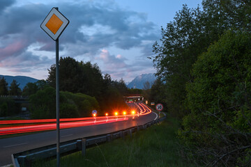 Cars driving on a winding mountain road at twilight, creating light trails, with a priority road...