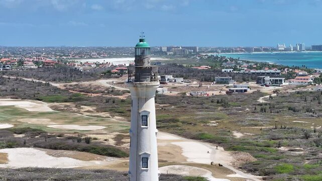 California Lighthouse At Oranjestad Caribbean Netherlands Aruba. Lighthouse Standing Tall On Beach With Ocean Waves Crashing. Coast Clouds Sky Seaside Summertime.