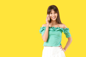 Young woman talking by mobile phone on yellow background