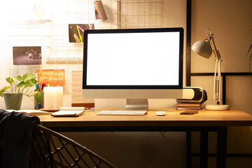 Workplace with blank computer monitor and glowing lamp in dark office