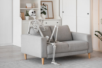 Human skeleton model sitting on grey sofa in living room
