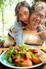 Indonesian teenage daughter embracing her father form behind, showing happy expression having lunch together at an outdoor restaurant