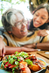 Indonesian teenage daughter embracing her father form behind, showing happy expression having lunch together at an outdoor restaurant