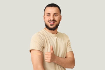 Young man with applied medical patch showing thumb-up on light background. Immunization concept