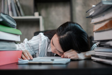 Tired student resting on a desk filled with books, symbolizing academic stress and fatigue in a study setting.
