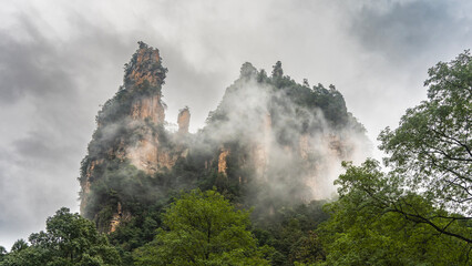 A picturesque mountain with bizarre outlines against the sky and clouds is shrouded in fog. Green...
